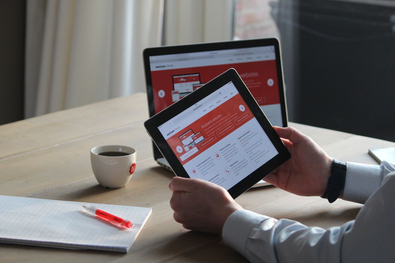 services-04 Business professional using a tablet and laptop with a hot drink, focusing on digital content review.