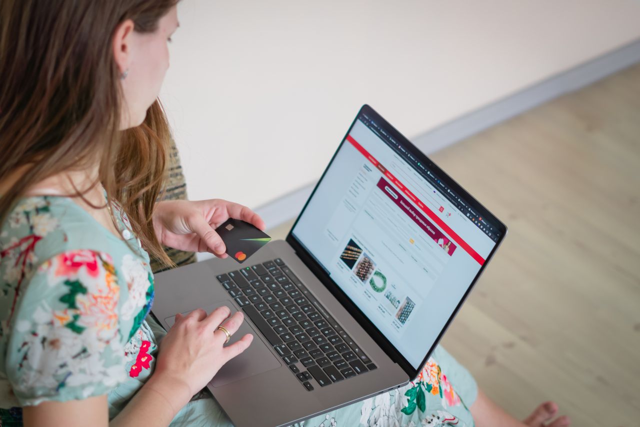 journey Woman in floral dress shopping online with a laptop and credit card indoors.